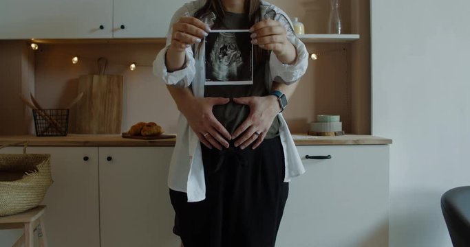 Pregnant women with her husband  Couple standing in kitchen and holding sonogram image in hands.  60 fps