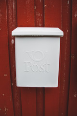 A white mailbox on a red wooden wall with a red door