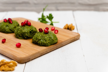 Spinach balls Pkhali with walnuts and served with pomegranate on white wooden background