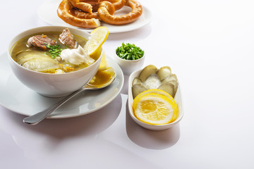 Soup Rassolnik with pickled cucumber, lemon and sour cream on a white background. Russian cuisine. Close up. Selective focus. For the menu.