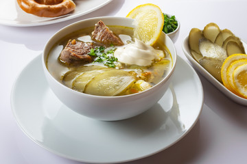 Soup Rassolnik with pickled cucumber, lemon and sour cream on a white background. Russian cuisine. Close up. Selective focus. For the menu.