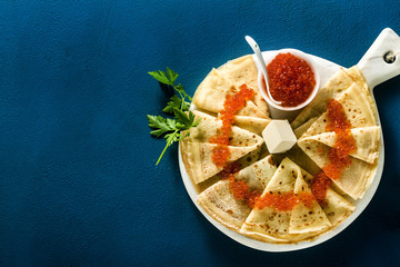 Traditional Russian pancakes with red caviar and butter on the blue table