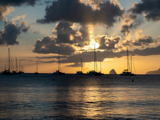 Sailboats in tropical laggon with the sunsetting behind the clouds and masts
