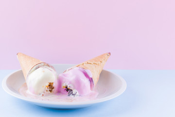 Melted ice cream on a pink blue background. Two ice cream cones on a white plate. Summer milk dessert in a waffle cone. Summer concept
