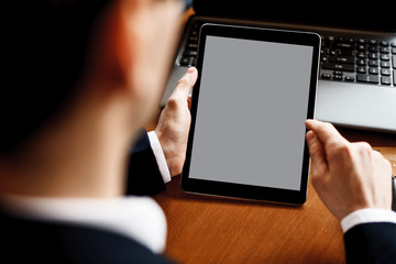 Male hands using a tablet while sitting at a desk with a laptop on it.