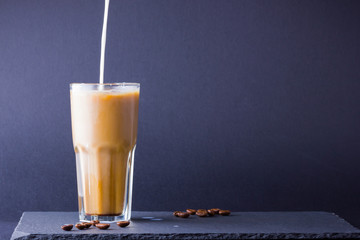 Iced coffee with milk on a dark background. Summer drink with caffeine on the slate board. Latte in...