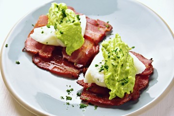 Paleo eggs benedict with avocado sauce on a bacon mat 