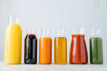 Glass bottles of fresh multicolored drinks standing in row on white background. Fruit and vegetable juice for you to drink. Healthy beverage