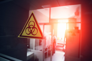 Biohazard symbol on glass of door to laboratory, selective focus with red light