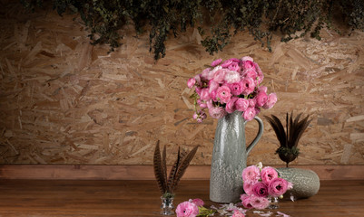 Pink roses in the vase on wooden table. Leaves dangling from the OSB board in the background.