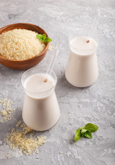 Organic non dairy rice milk in glass and wooden plate with rice seeds on a gray concrete background.