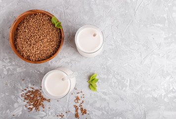 Organic non dairy buckwheat milk in glass and wooden plate with buckwheat seeds on a gray concrete background.