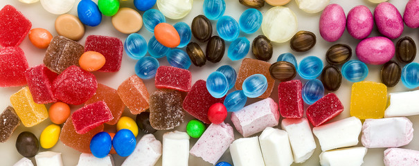 banner of multicolored caramel candies scattered on the table background. sugar products. colored sweets