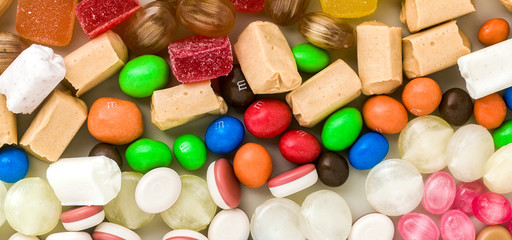 banner of multicolored caramel candies scattered on the table background. sugar products. colored sweets