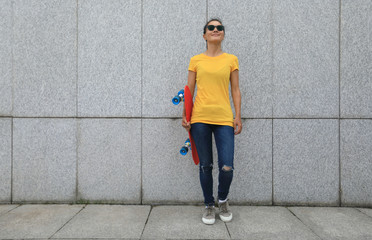 Woman skateboarder withe skateboard stand against walll at city