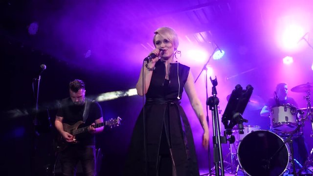 Female singer performs on the stage with guitarist, bass and drummer.