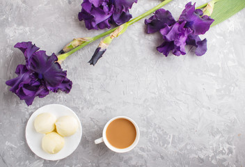 Purple iris flowers and a cup of coffee with marshmallow on a gray concrete background.