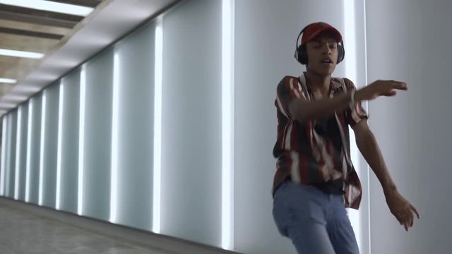 young handsome attractive latin guy walks in the neon light of the night city listens to music with wireless headphones and dances