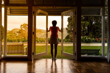 Woman opening glass door to refreshing sunrise with greenaries