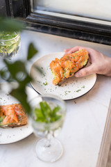 Black bread bruschetta with cheese, cucumber and slices of red fish of fresh salmon. Laid on white plates and sprinkled with green onions. In glass glasses water with mint leaves. Summer cafe.