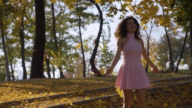 extra long shot. funny curly girl in the park girl spinning among the golden trees. warm autumn day, soft light. 4K