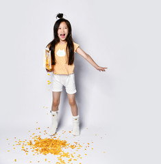 Beautiful asian girl kid at the morning breakfast pouring out corn flakes yawning on gray 