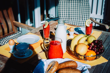 Continental Breakfast with fresh juice, milk, fruits and eggs set on a garden table outdoors.