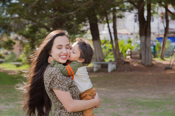 Cute two year old boy kissing his young mother while they both smile and have fun