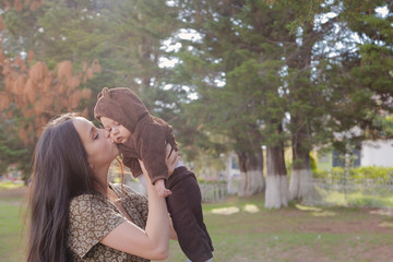 Pretty mom kissing her baby in the park surrounded by trees on a sunny afternoon