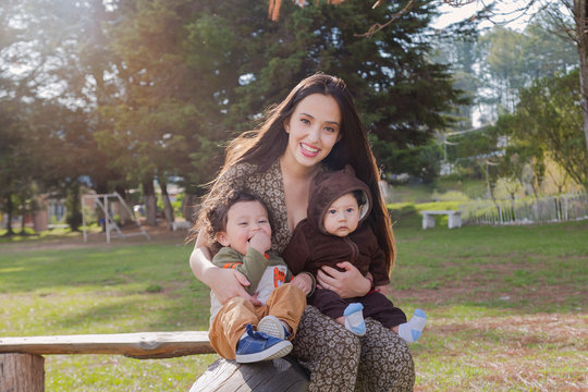 Portrait of young mother with her two small children smiling and having fun in the park outdoors