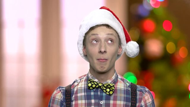 Funny teen boy in Christmas hat. Cute teenage guy in Santa Claus cap looking thinking on abstract Christmas background. Winter holidays concept.