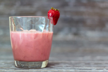 Glass with natural strawberry milkshake on rustic background
