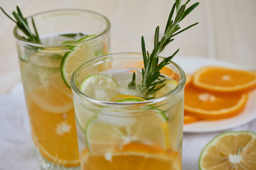 Two glasses of cool refreshing drink with ice, orange and rosemary on a white napkin, close-up