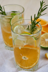 Two glasses of cool refreshing drink with ice, orange and rosemary on a white napkin