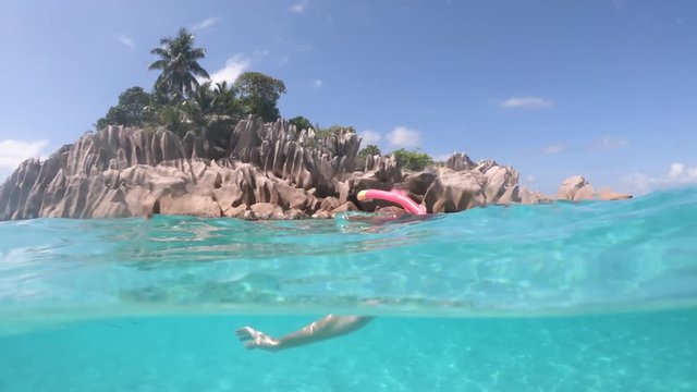 Split view of female apnea under and above the sea. Snorkeling dress woman at St. Pierre Island near praslin, Seychelles. Travel lifestyle watersport activity. Fishes and sealife in foreground.