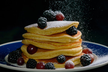 Stacked pancakes with summer berries and falling confectioners sugar