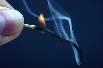 Burning and smoking wooden match in hand on dark background