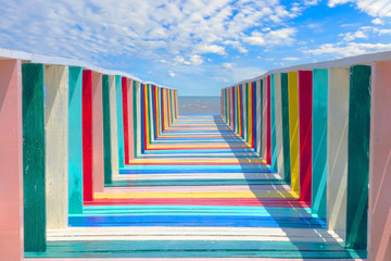 The colorful wood bridge extends into the sea in Cloudy sky - obrazy, fototapety, plakaty