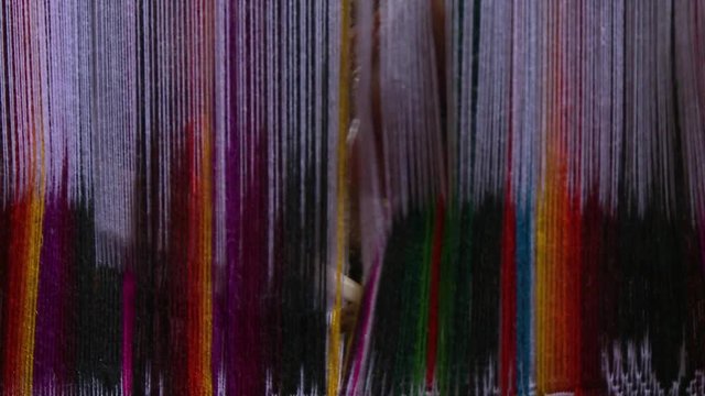 Handheld, extreme closeup shot of hands threading colorful strings of fabric from back angle.