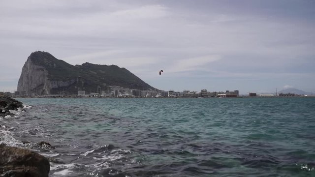 Handheld shot of rock of Gibraltar, with sea in foreground and kitesurfer