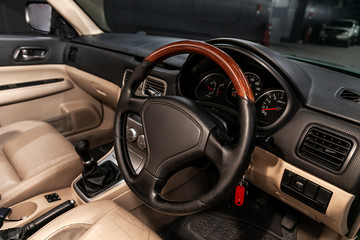 Close-up of the dashboard, speedometer, tachometer and steering wheel with wooden inserts with phone setting and volume buttons. Luxurious car interior details.