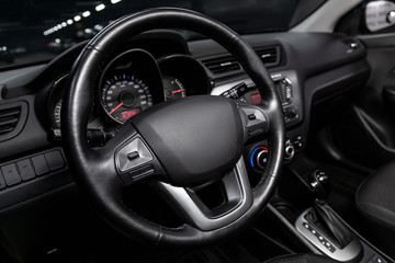 Close-up of the dashboard, speedometer, tachometer and steering wheel with phone setting and volume buttons. Luxurious car interior details.