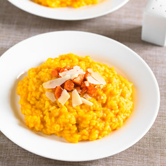 Fresh homemade carrot risotto made with pureed carrot, garnished with roasted carrot and hard cheese, photographed with natural light (Selective Focus, Focus in the middle of the image)
