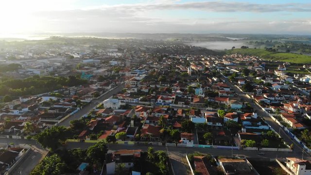 Aerial view of a yellow bus and a low-income urban area in Cruz das Almas, Bahia, Brazil. Show houses, small buildings in the neighborhood, and green environnement. Drone slowly moving down.