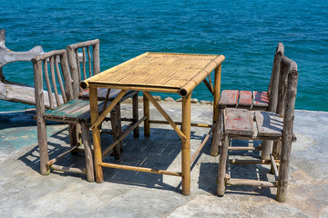 Obraz na płótnie Canvas Bamboo table and wooden chairs in empty cafe next to sea water in tropical beach . Island Koh Phangan, Thailand
