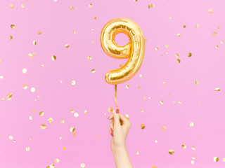 Nine year birthday. Female hand holding Number 9 foil balloon. Nine-year anniversary background. 3d...