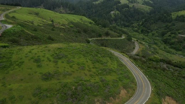 Aerial pull back shot of a very windy section of highway 1 in northern California with cars driving past.