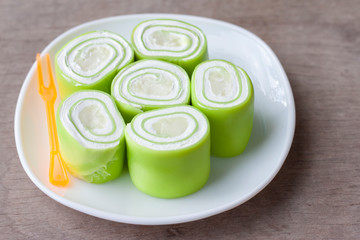Young coconut pandan roll cake in white plate on vintage wooden table background.