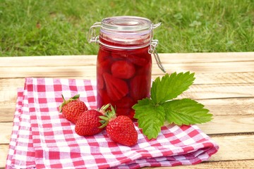 Strawberry jam in glass jar  and fresh strawberries on a wooden table with a red checkered napkin on a green vegetable background.Homemade jam.Summer berry jam. Canned berries. Healthy vegetarian 