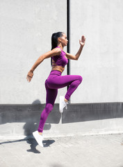 Woman athlete in motion jumps on the background of the city wall.  Sports girl fit exercising outdoors. Fitness training.